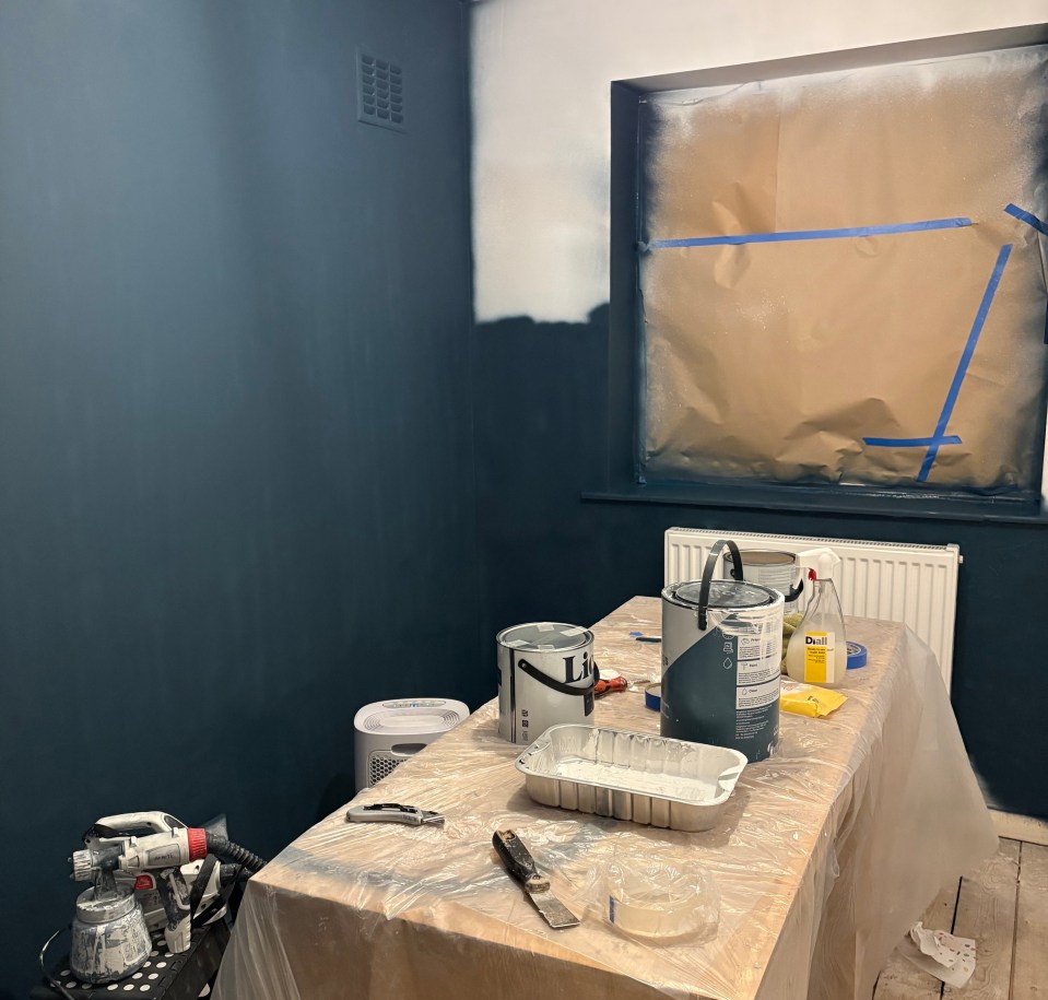 Room being painted with paint sprayer and supplies on a table.