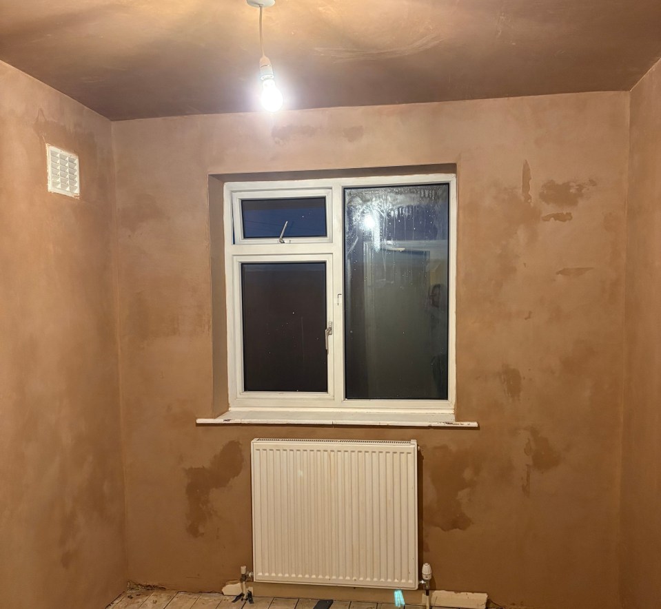 Room with newly plastered walls and ceiling, wood floor, radiator, and window.