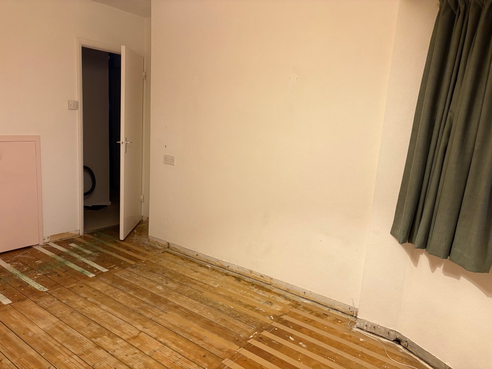 Room with exposed wooden floor and damaged baseboards.