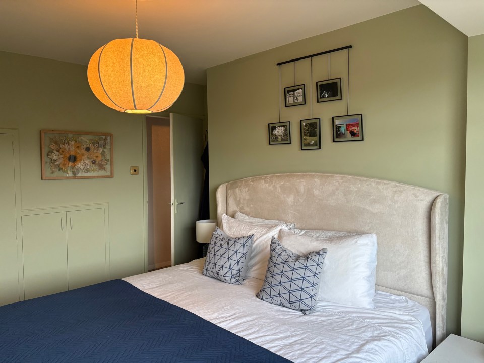 Bedroom with a beige headboard, navy blue blanket, and framed photos on the wall.