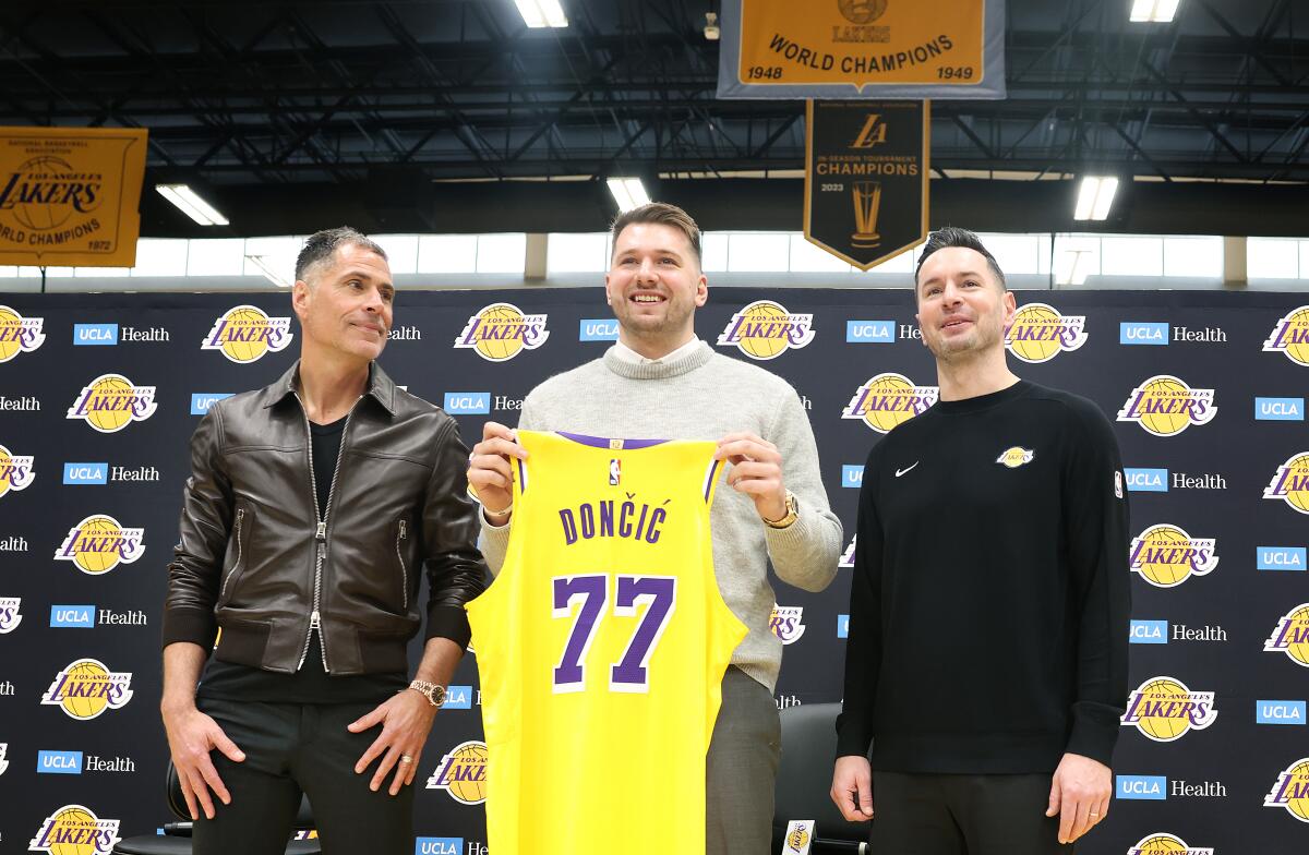 Luka Doncicposes for a photo holding his new Lakers jersey while flanked by GM Rob Pelinka, left, and coach JJ Redick, right.