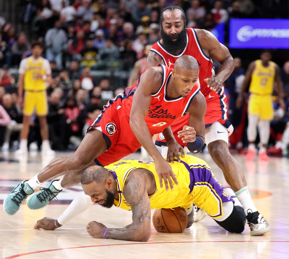 LeBron James of the Lakers battles for a loose ball with Clippers Kris Dunn (foreground) and James Harden.