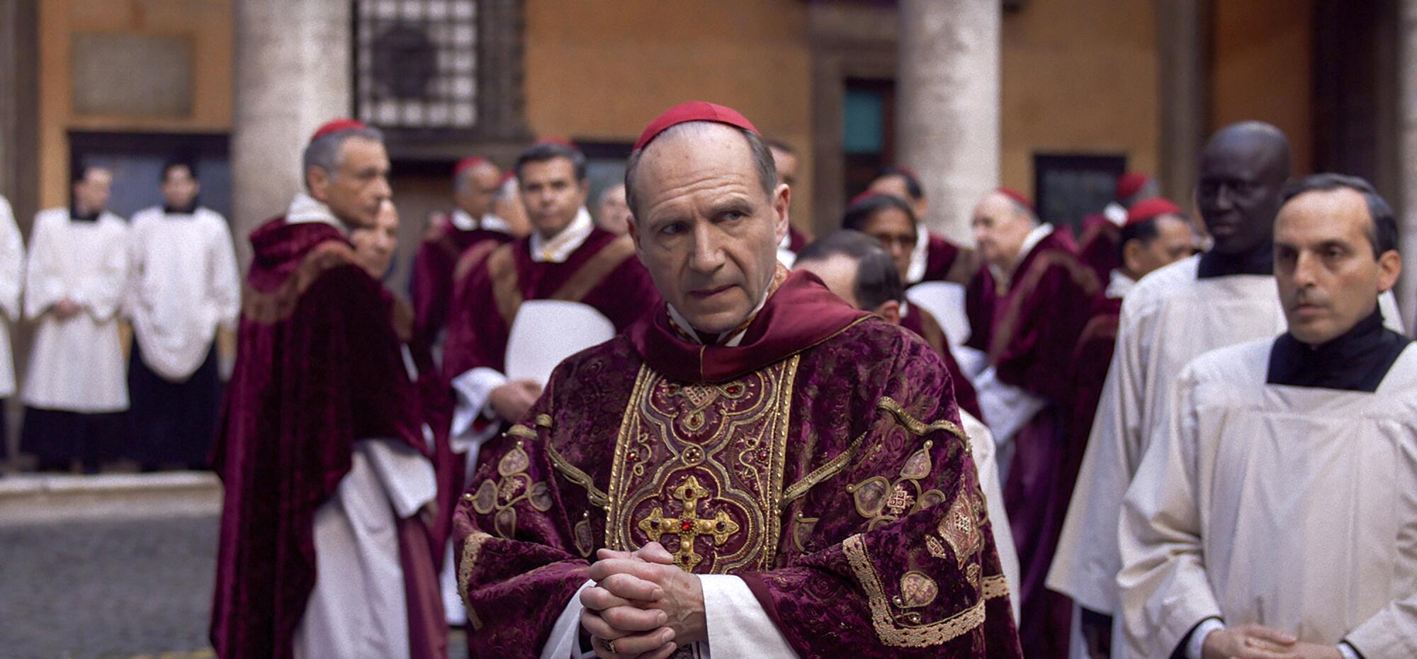 A man in cardinal's robes stands amid other members of the clergy in "Conclave."