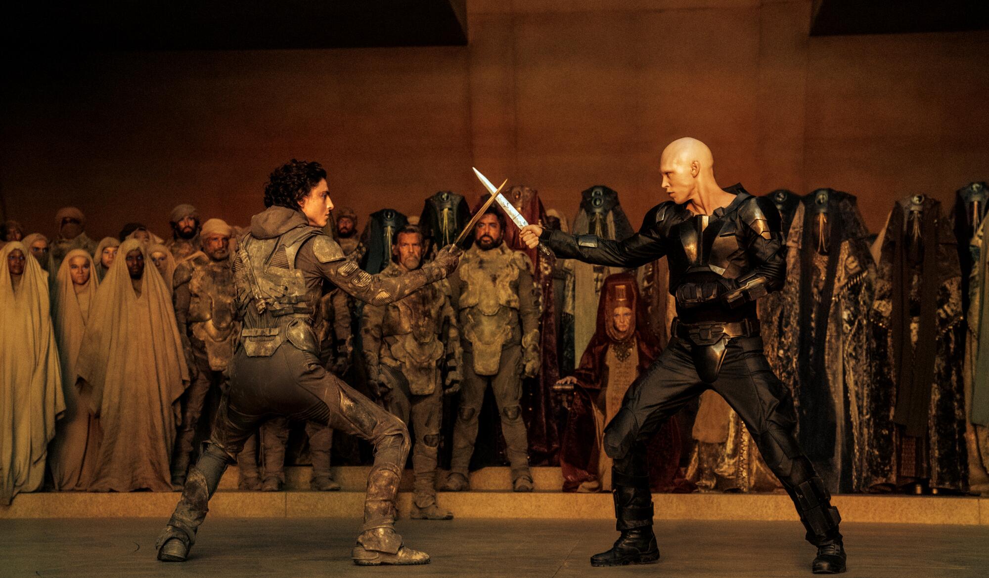 Two men in unusual garments fight with swords in front of a crowd in "Dune: Part Two."