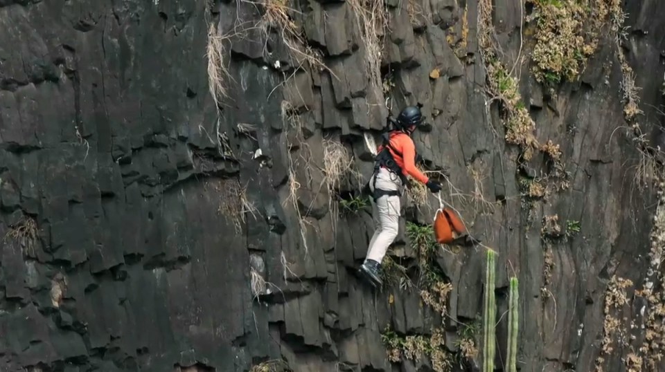 Person rappelling down a rocky cliff face.