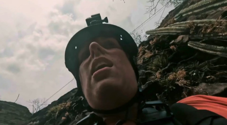 Close-up of a person wearing a helmet and GoPro, appearing to have crashed into a cliff.