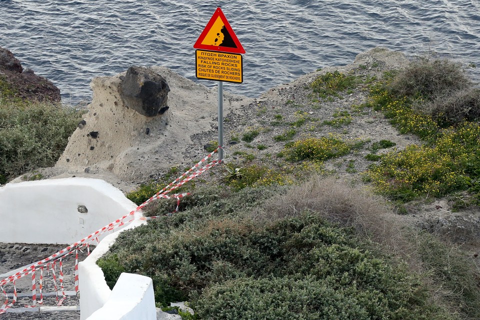 Warning sign for falling rocks near a cliff in Santorini, Greece.