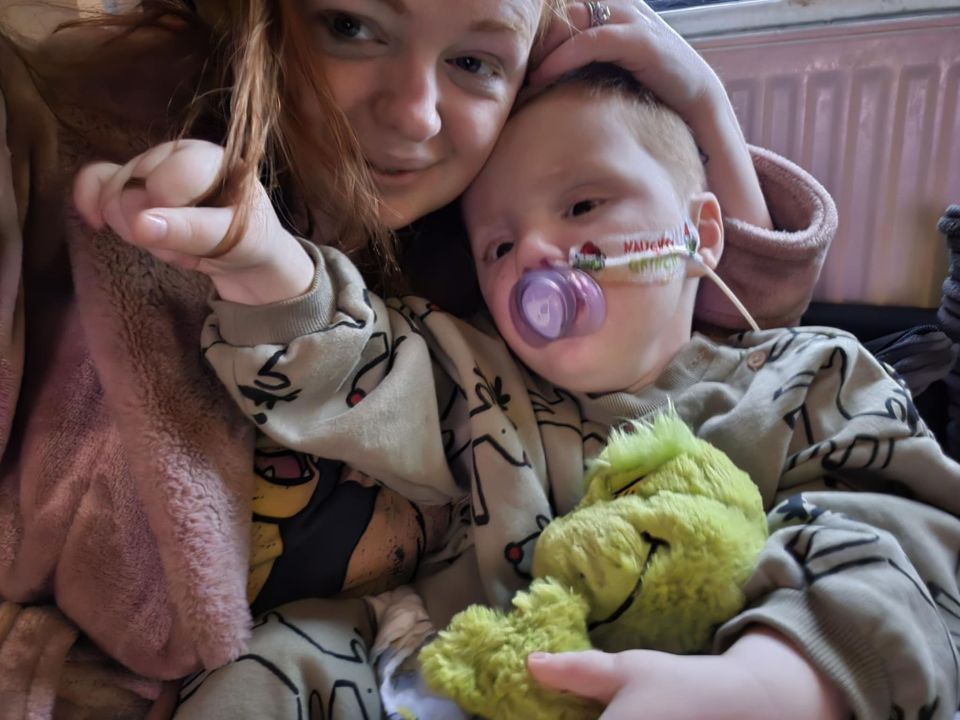 A mother holding her young son, who has a nasal cannula and pacifier.