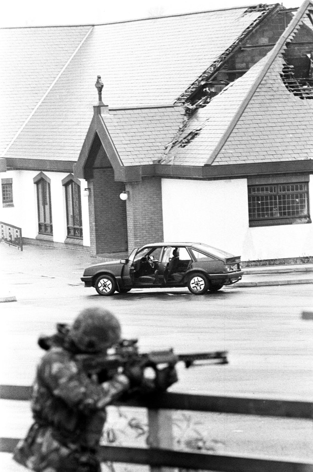 Aftermath of an IRA shootout: a damaged building, getaway car, and soldier with a rifle.