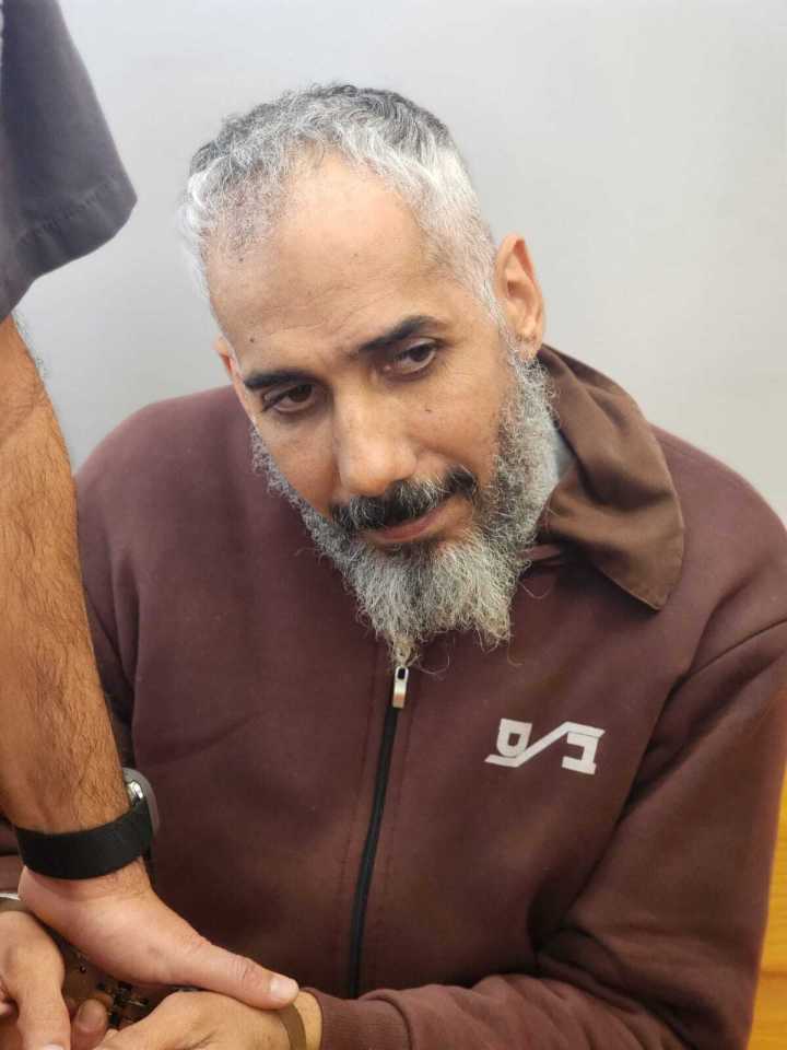 Close-up of a man with graying hair and beard, wearing handcuffs.