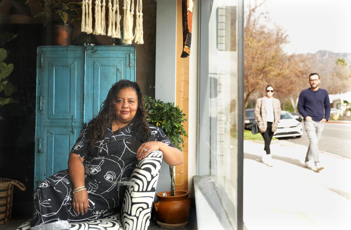 A woman sits next to a window inside a bookstore. A man and a woman walk on the sidewalk outside.