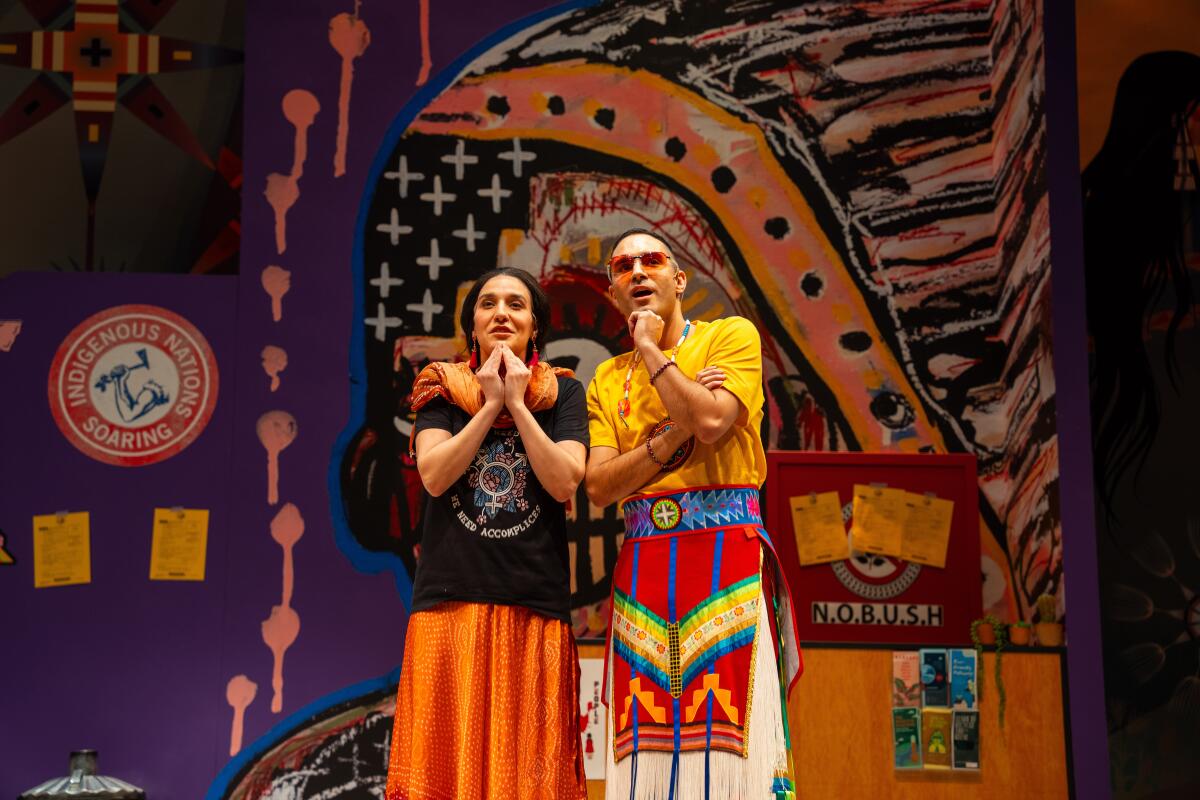 Two people in colorful Native American-themed costumes stand onstage