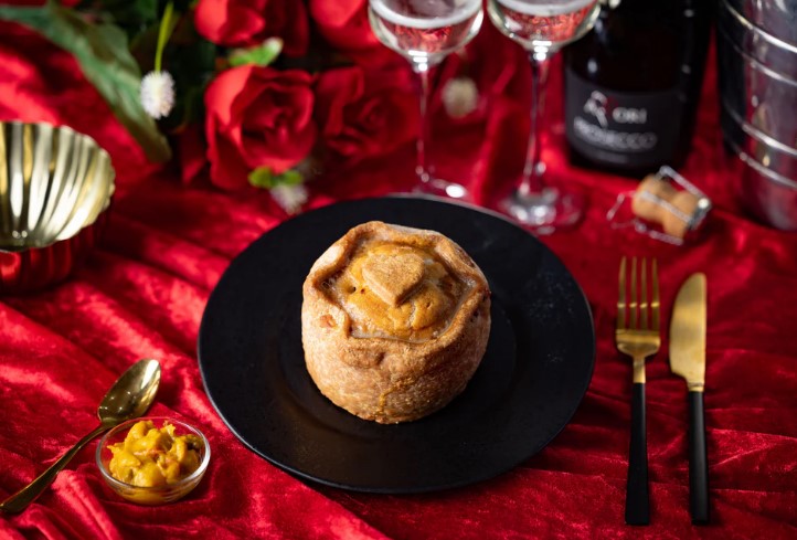 A heart-shaped pork pie on a black plate, with champagne flutes and roses in the background.