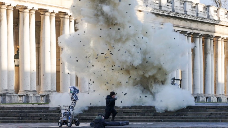 A film still of an explosion scene with an actor running away from the blast.