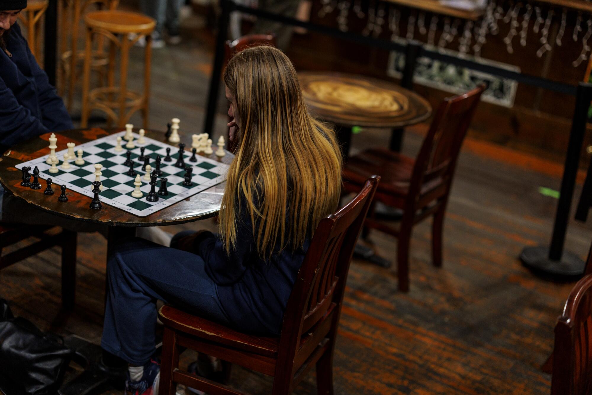 Two people seated at a circular table play chess. 