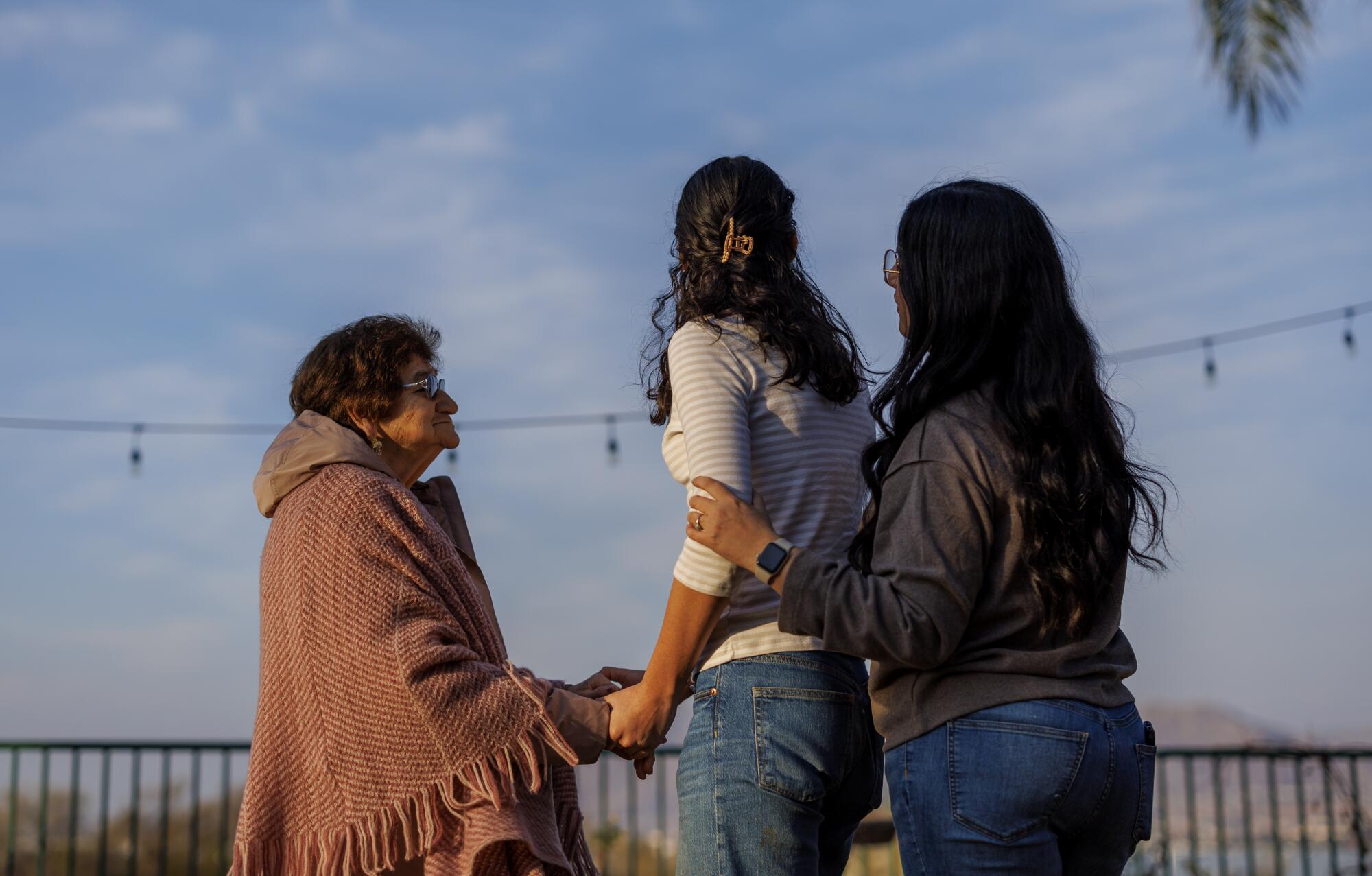 Three people join hands outdoors. 