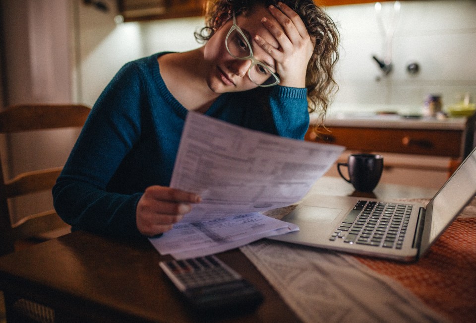 Woman looking stressed while reviewing bills at her kitchen table.