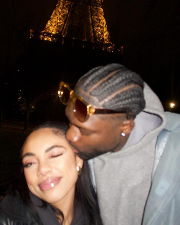 A man kissing a woman on the cheek in front of the Eiffel Tower at night.