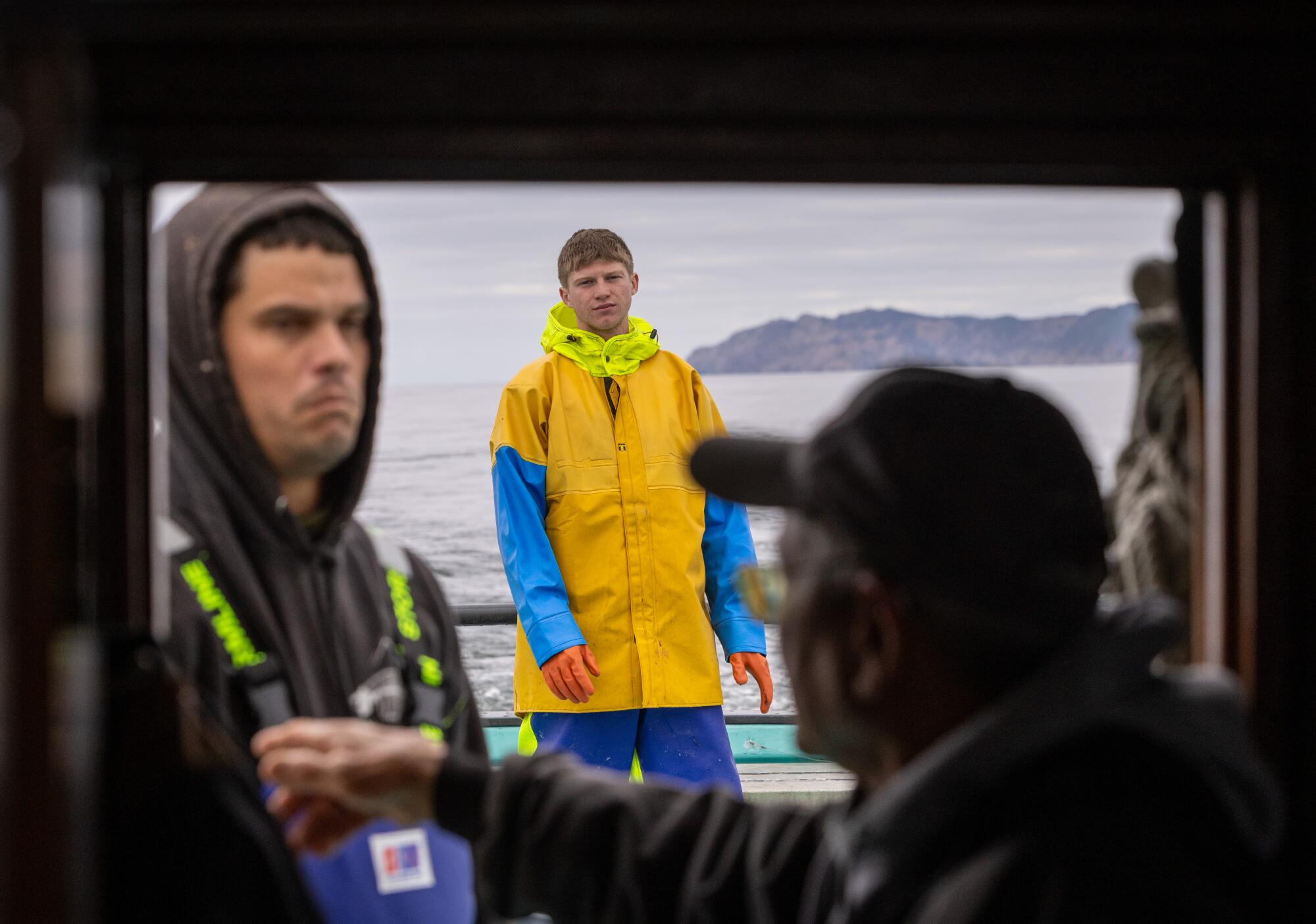 A boat captain seated at the helm gives instructions to his crew.