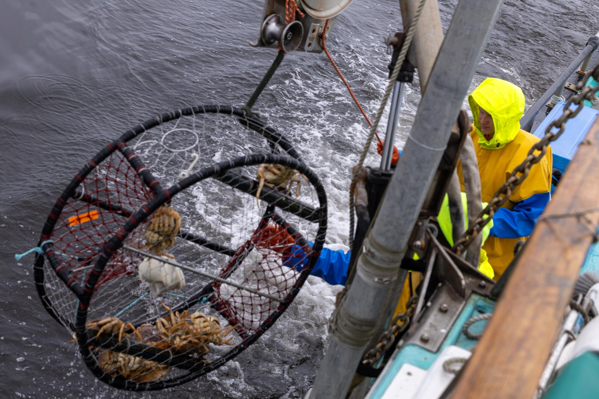 Two crew members on a fishing boat pull a crab pot from the Pacific Ocean.