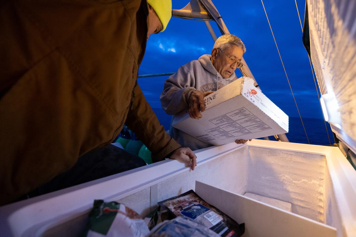 Two men place boxes of frozen bait into a freezer on a fishing boat.  