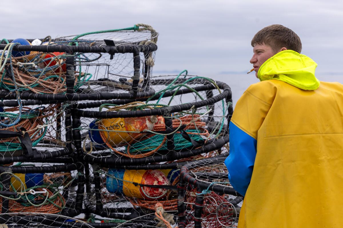 A man in yellow coveralls stacks crab pots on a boat.