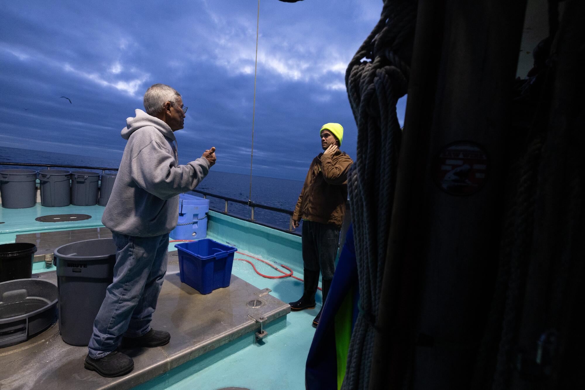 A captain and crew member stand on the deck of a crabbing boat under dark skies. 