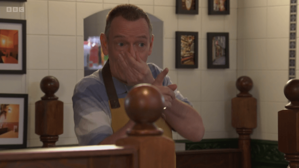 Man in a blue shirt and apron covering his nose and mouth.