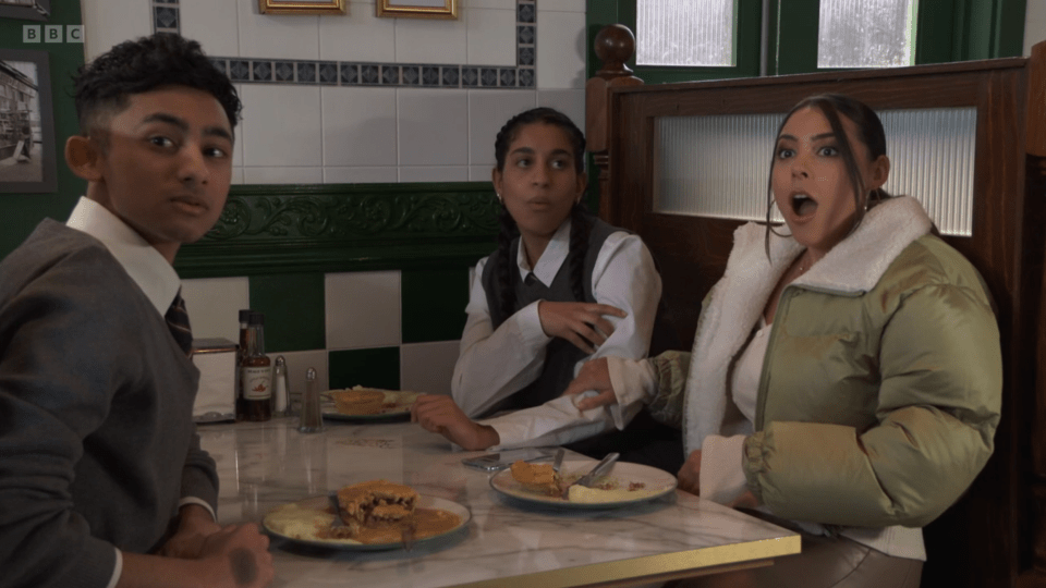 Three people sitting at a table in a cafe, eating pies.