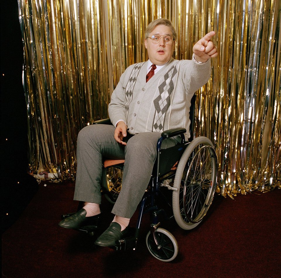 Peter Kay in a wheelchair, pointing.