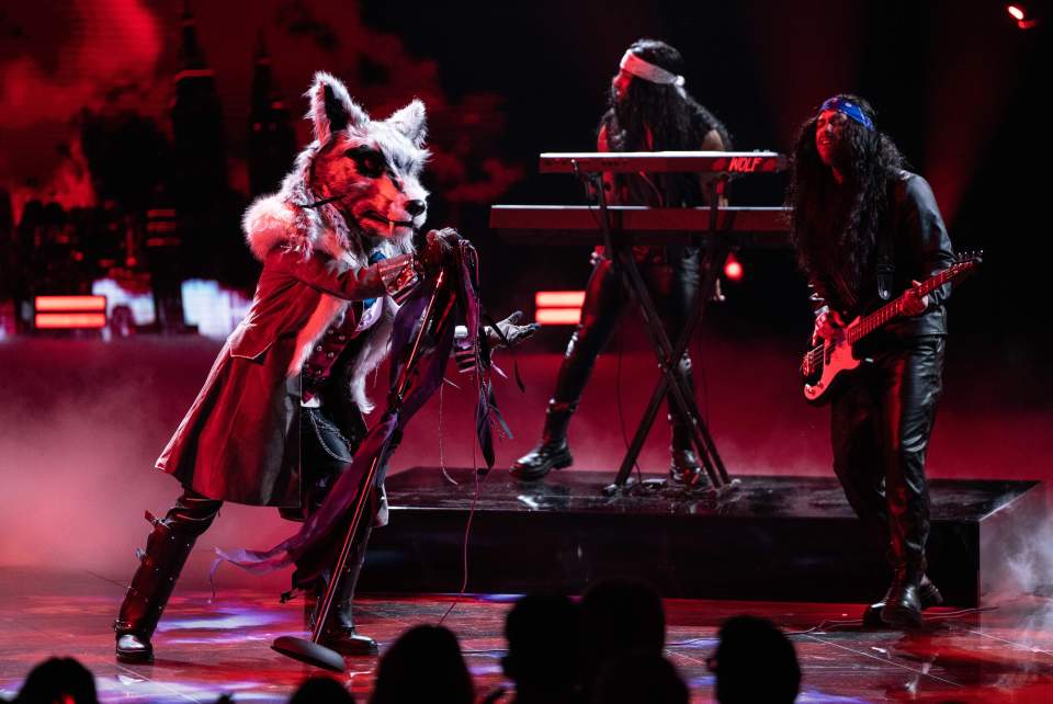 Wolf, a contestant on The Masked Singer, performing on stage with a band.