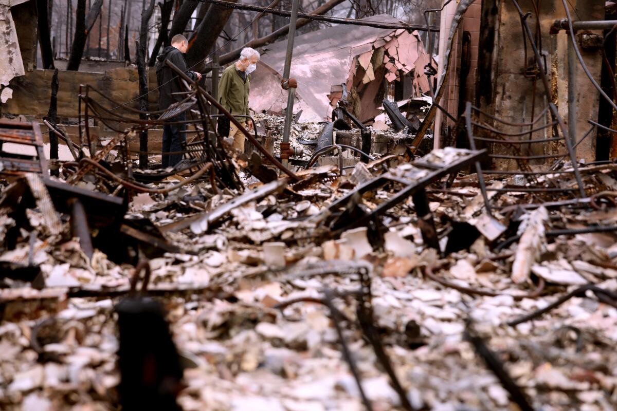 A pair of men stand in the middle of a fire damaged home

