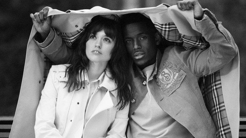 Black and white photo of a couple sharing a Burberry trench coat.