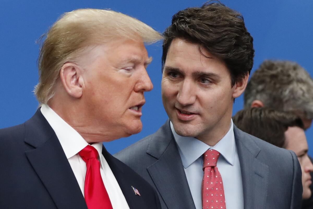 A blond-haired man, left, speaks to a man with dark hair, who is also wearing a suit and red tie