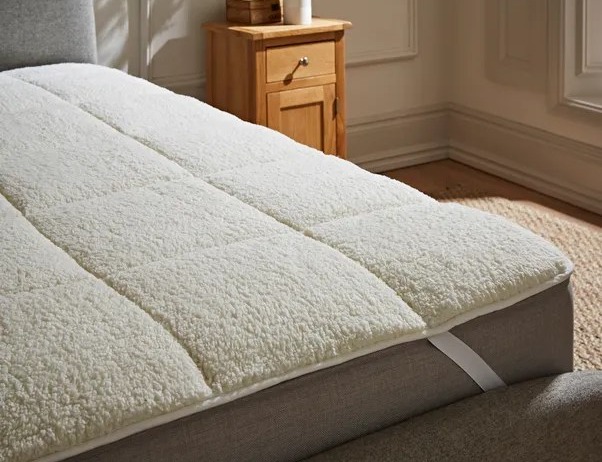 Cream-colored fleece mattress topper on a bed.