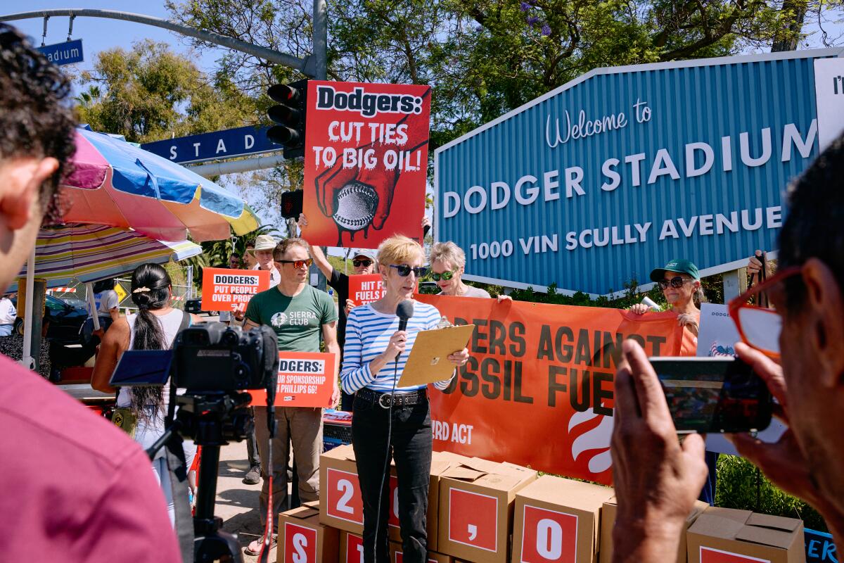 People, some holding signs, gather near a woman speaking while holding a microphone