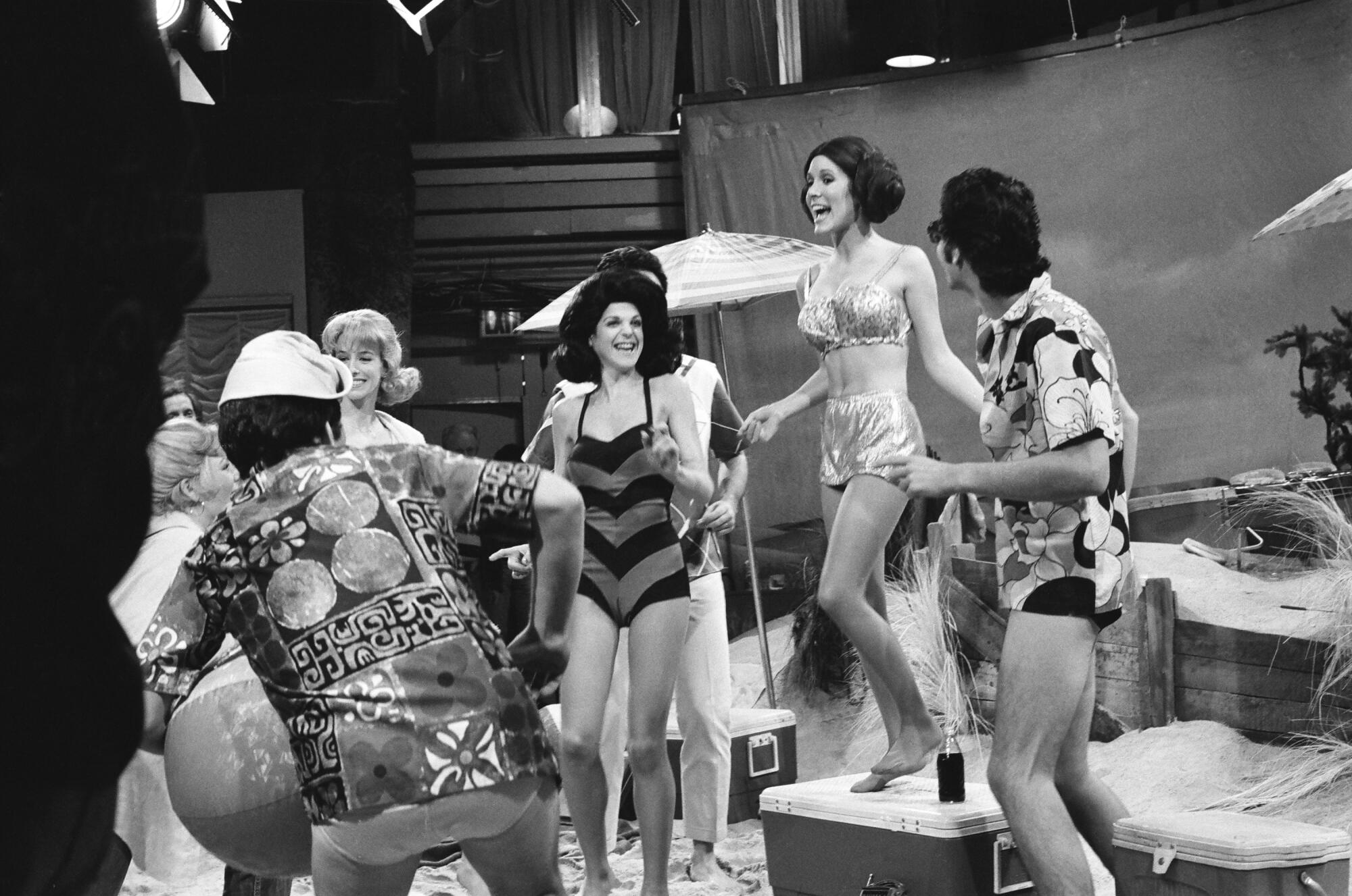 A black and white photo of women and men in swimsuits on a staged beach.