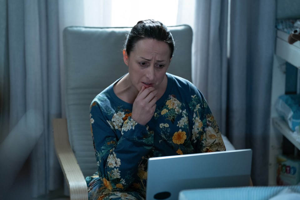 A worried woman sits in a chair looking at a laptop.