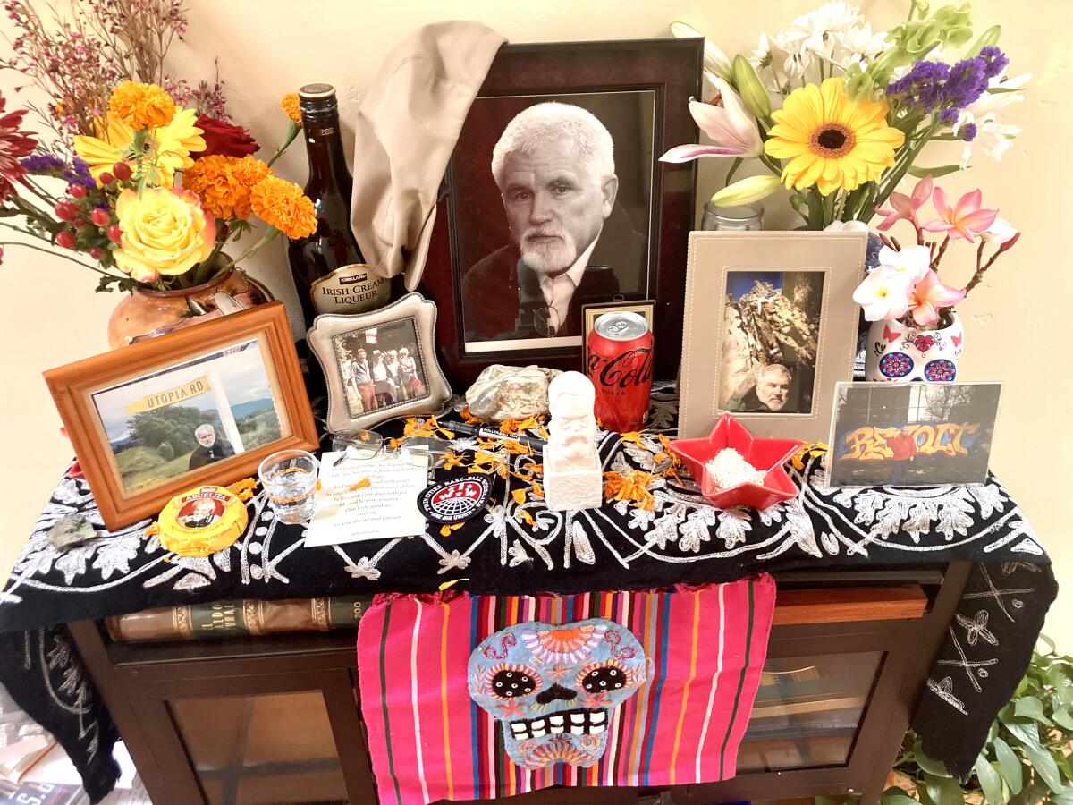 A Dia de Muertos altar with bright textiles features flowers, photos of Mike Davis, Abuelita hot chocolate and a can of Coke