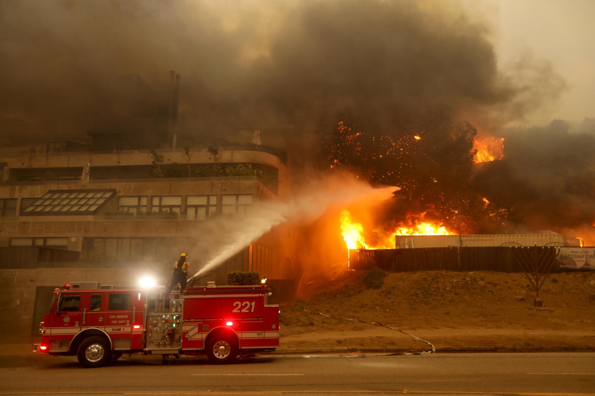 A firefighter tries to put out a portion of the Pacific Palisades fire that threatens a nearby building