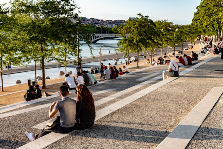 The banks of the Rhone at Lyon. There are groups of young people sitting on the steps beside the promenade along the banks of the river.