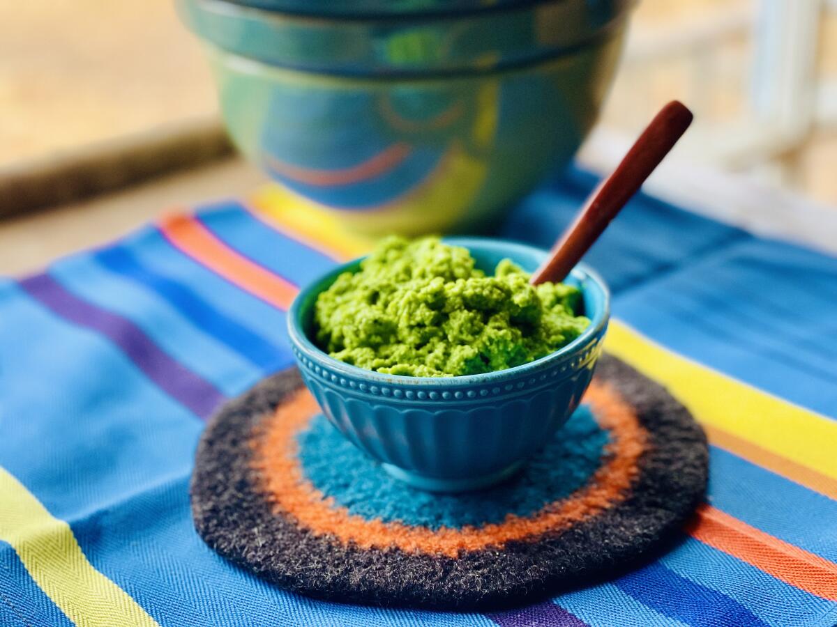 Sweet pea guacamole in a blue bowl on a blue, yellow, orange and purple tablecloth.