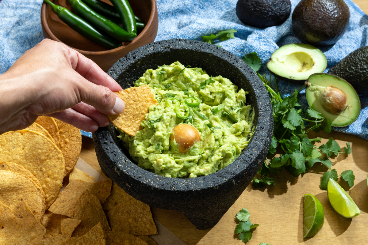 A hand scoops a tortilla chip into a bowl of guacamole.