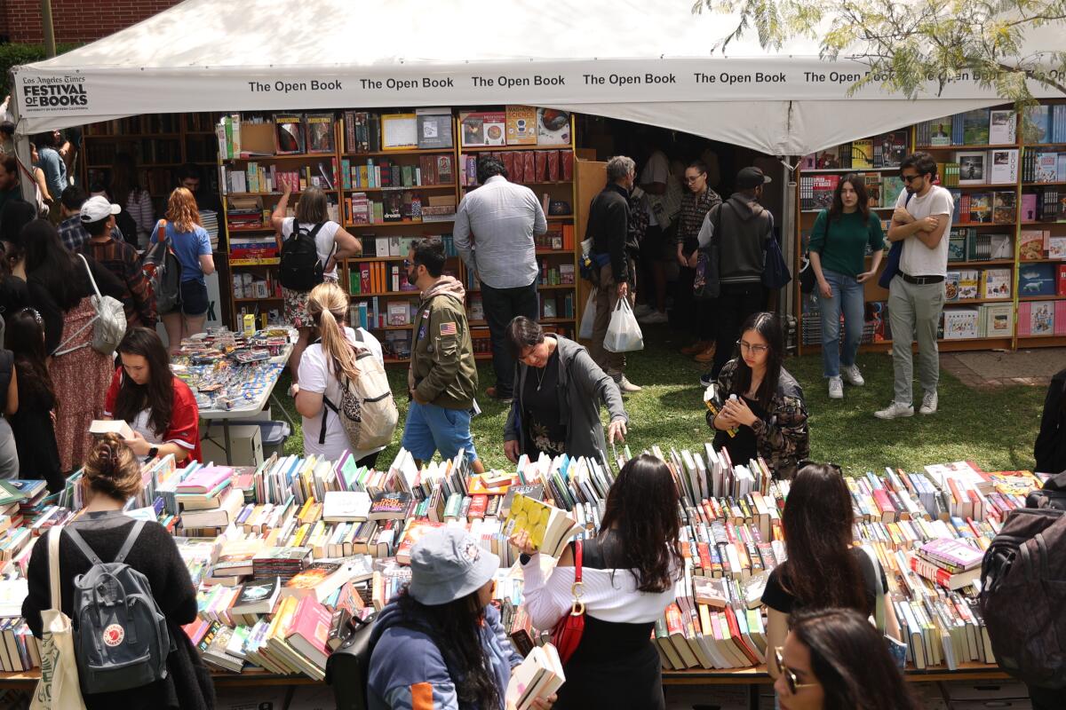 People looking through book stacks on tables and bookshelves under a tent