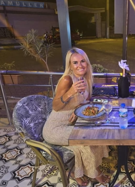 Woman sitting at an outdoor restaurant table, raising a glass of wine.