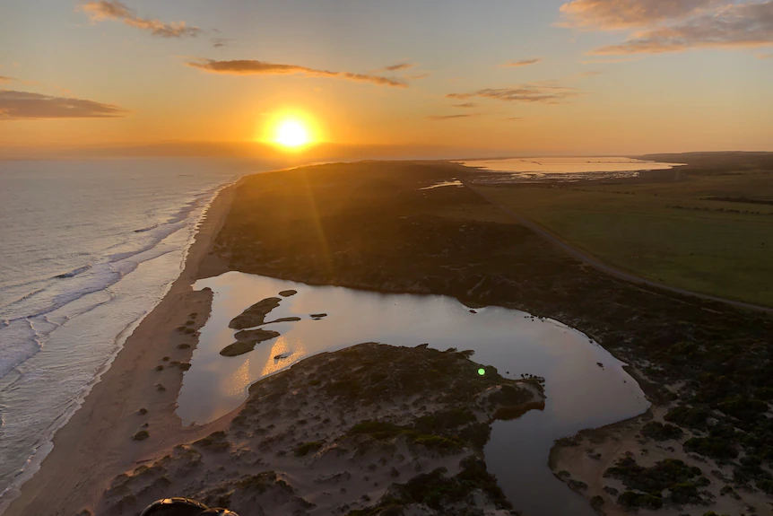 An aerial shot of a beach with the sun low on the horizon.