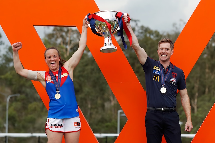 Daisy Pearce and Mark Stinear smile as they hold up the premiership cup
