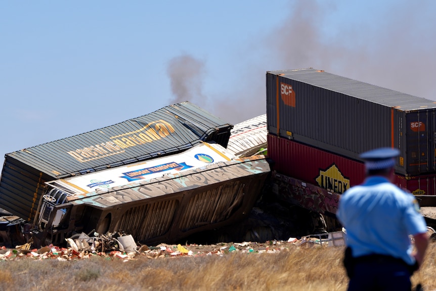 The back of a police officer looking towards damaged and overturned carriages