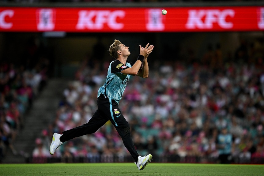 A man runs after a cricket ball about to catch it.