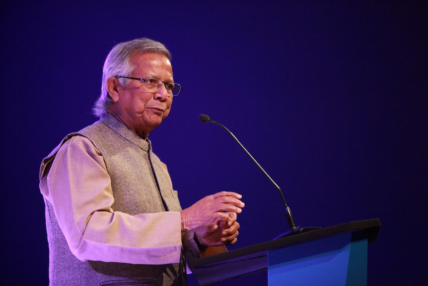 A man stands at a lecturn in front of a microphone.